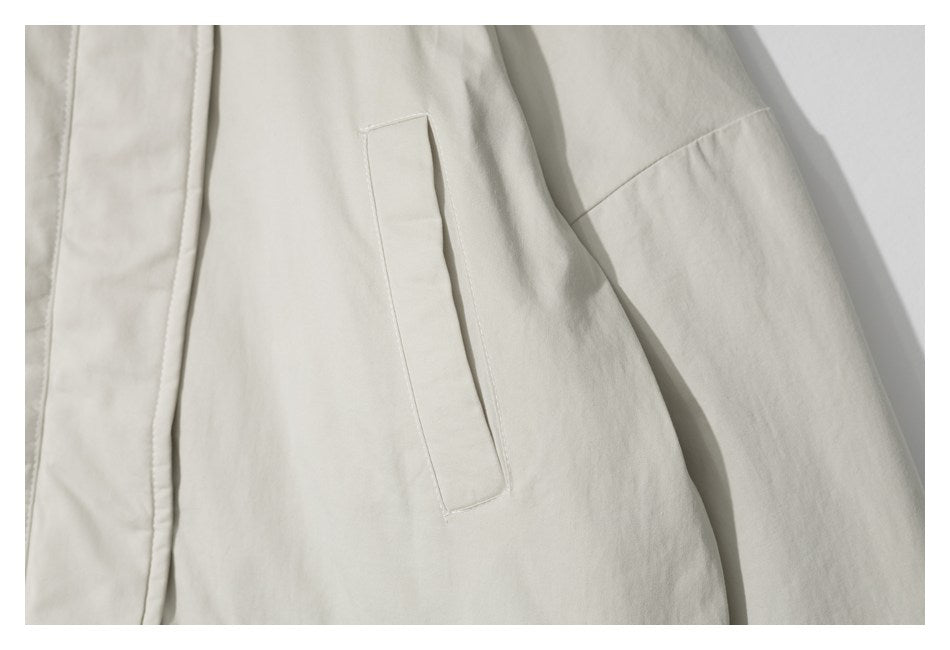 Close-up of an off-white jacket showing a narrow welt pocket and sleeve seam.