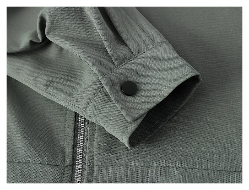 Close-up of a gray-green jacket sleeve cuff with a black snap fastener and metal zipper nearby.