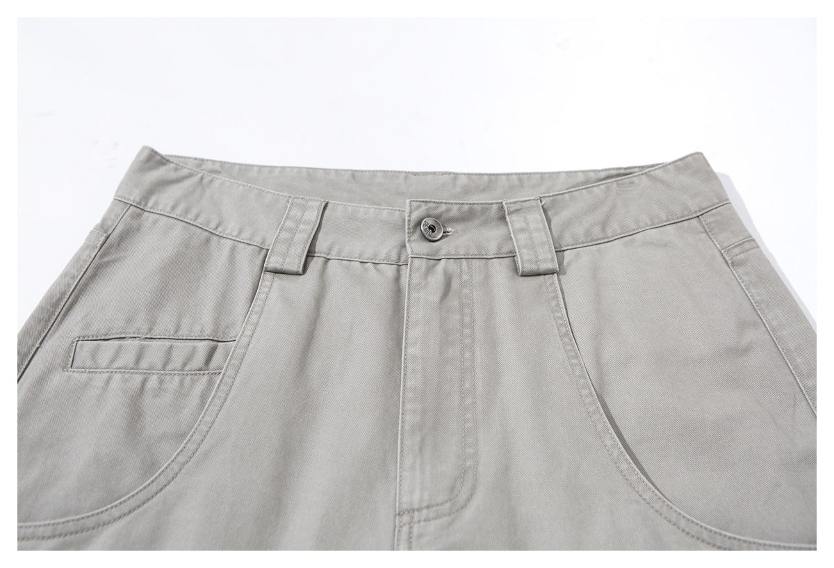 Close-up of light gray trousers showing the front waistband, button, belt loops, fly, and curved pockets.