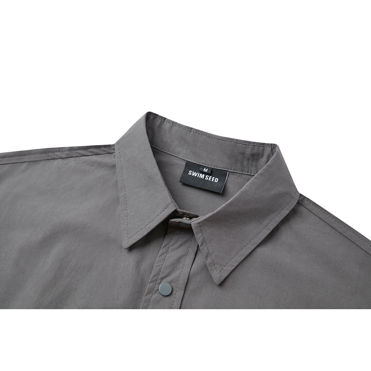 Close-up of a gray short-sleeve shirt’s pointed collar, snap-button placket, and SWIM SEED neck label.