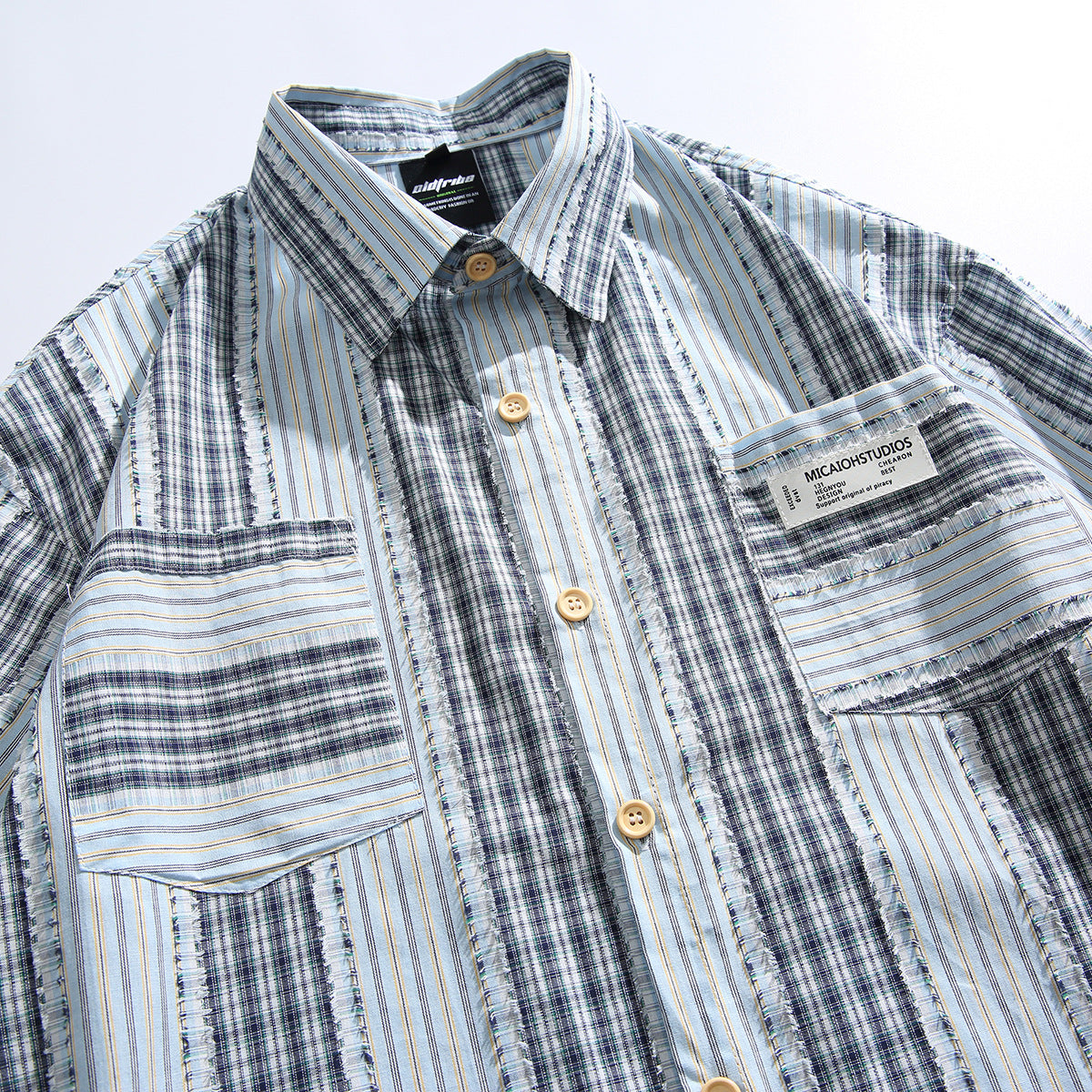 Front close-up of a short-sleeve button-up shirt with blue, navy, and white striped plaid panels and two chest pockets.