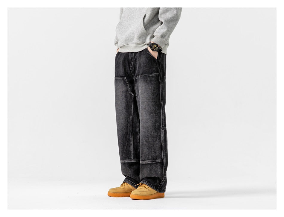 Side-angle view of model wearing black wide-leg paneled jeans with a gray hoodie and tan sneakers