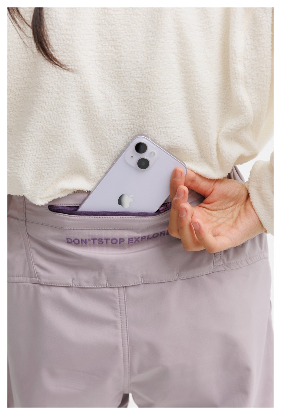 Close-up of a lavender trouser waistband pocket holding a phone, with “DON'T STOP EXPLORE” printed on the waistband.