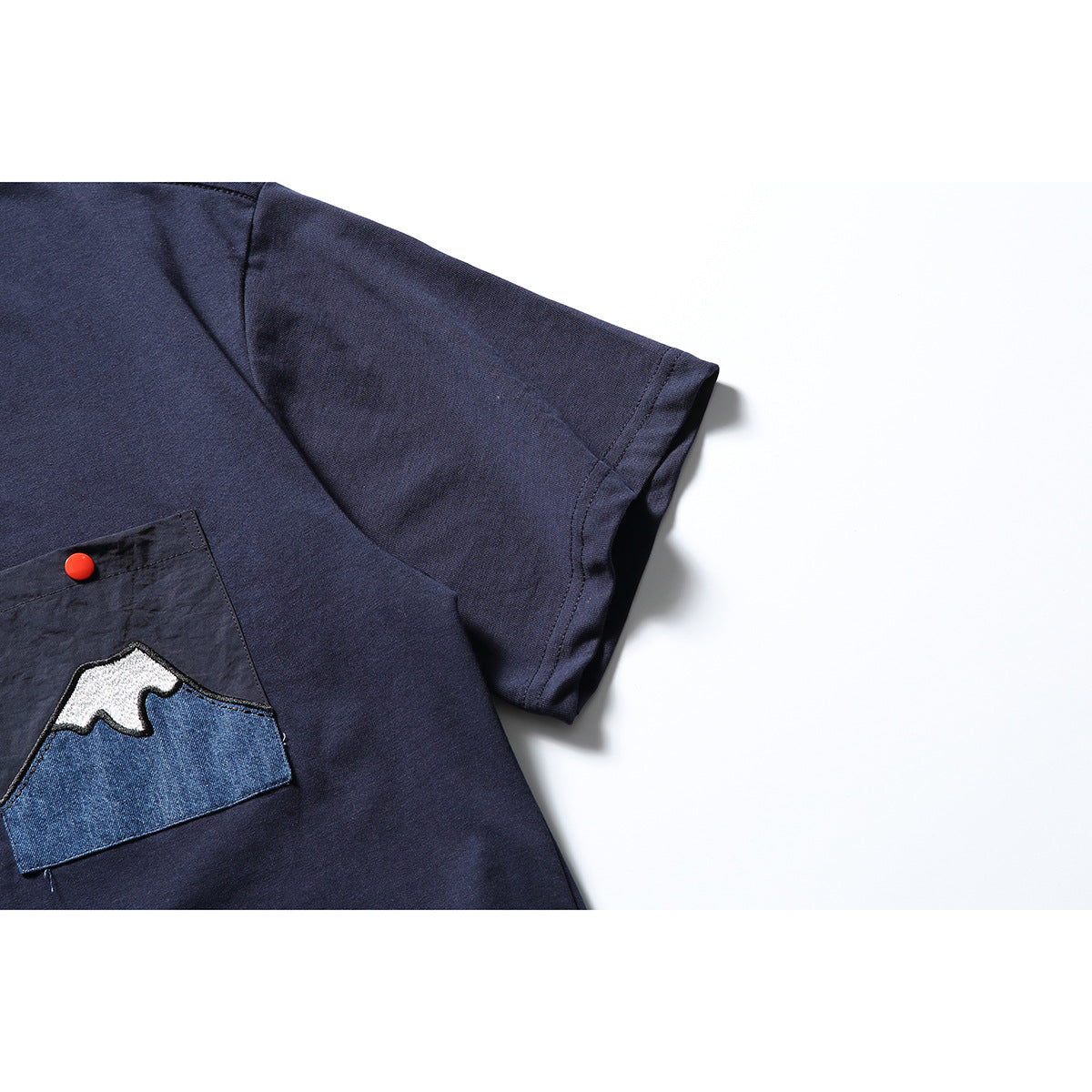 Close-up of the navy T-shirt sleeve and chest pocket with a red snap and mountain appliqué.