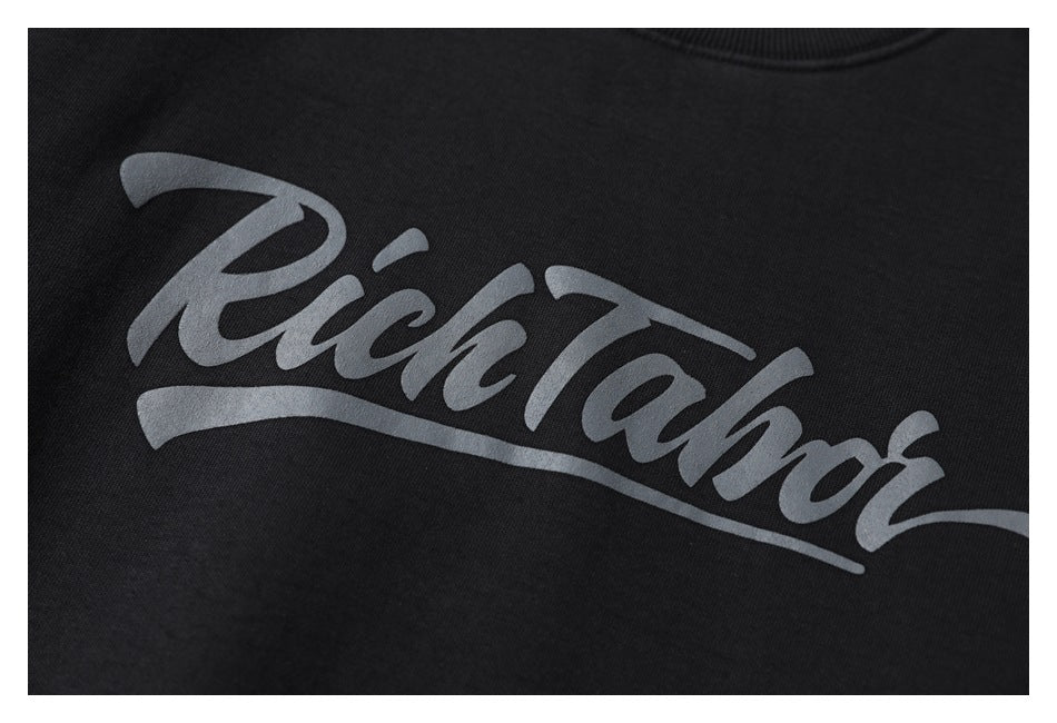 Close-up of gray script lettering printed on the black sweatshirt.