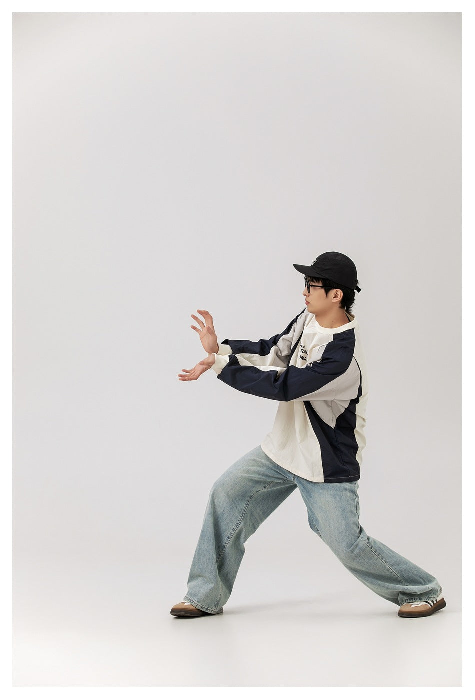 Model in a navy-and-ivory color-block long-sleeve top, shown in a side-facing pose with arms extended.