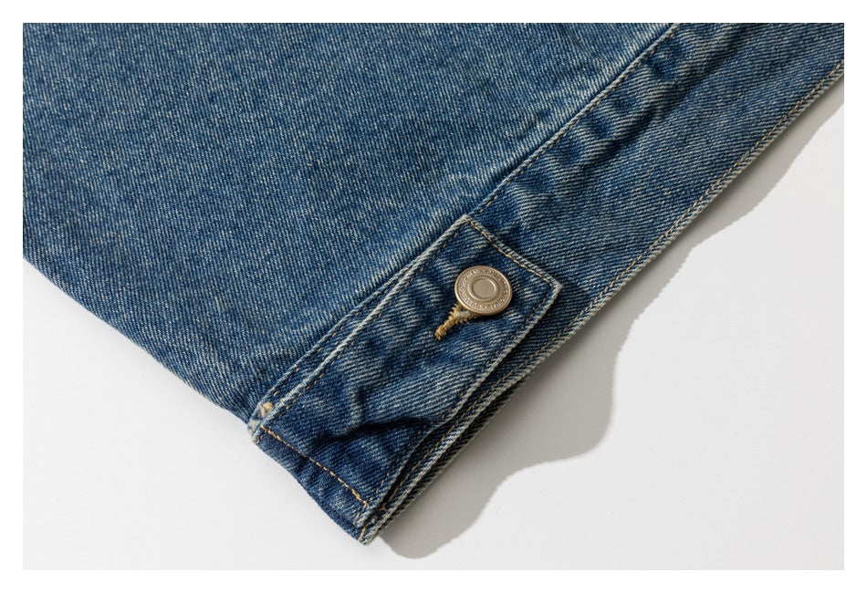 Close-up of a blue denim jacket hem tab with a metal button and tan stitching.
