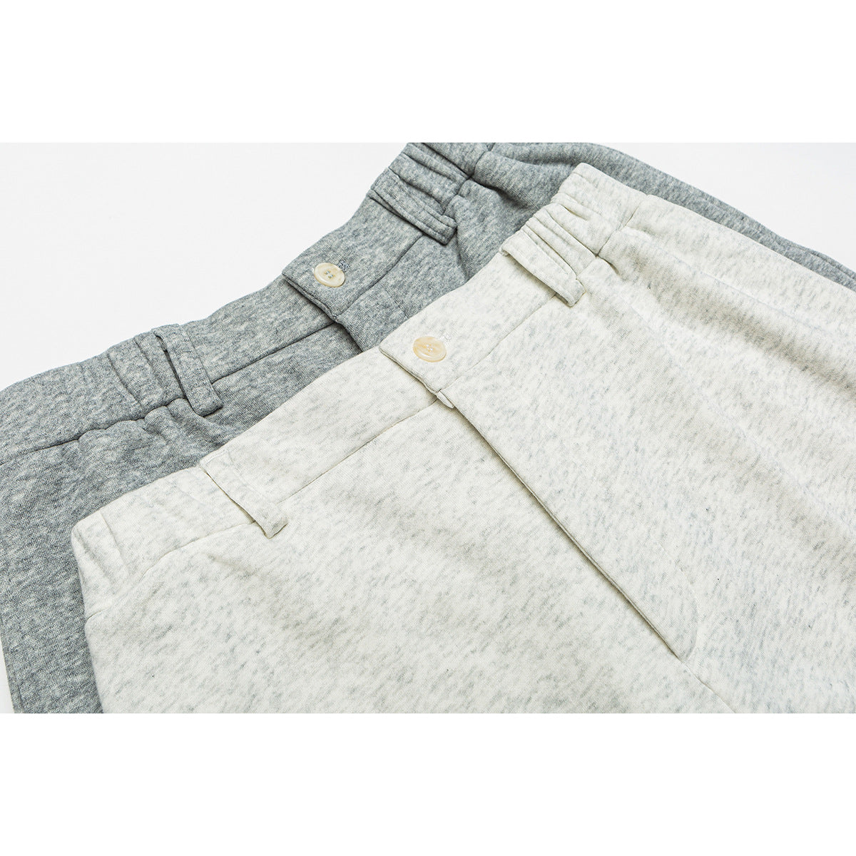 Close-up of ivory and heather-gray trousers showing buttoned waistbands and belt loops.