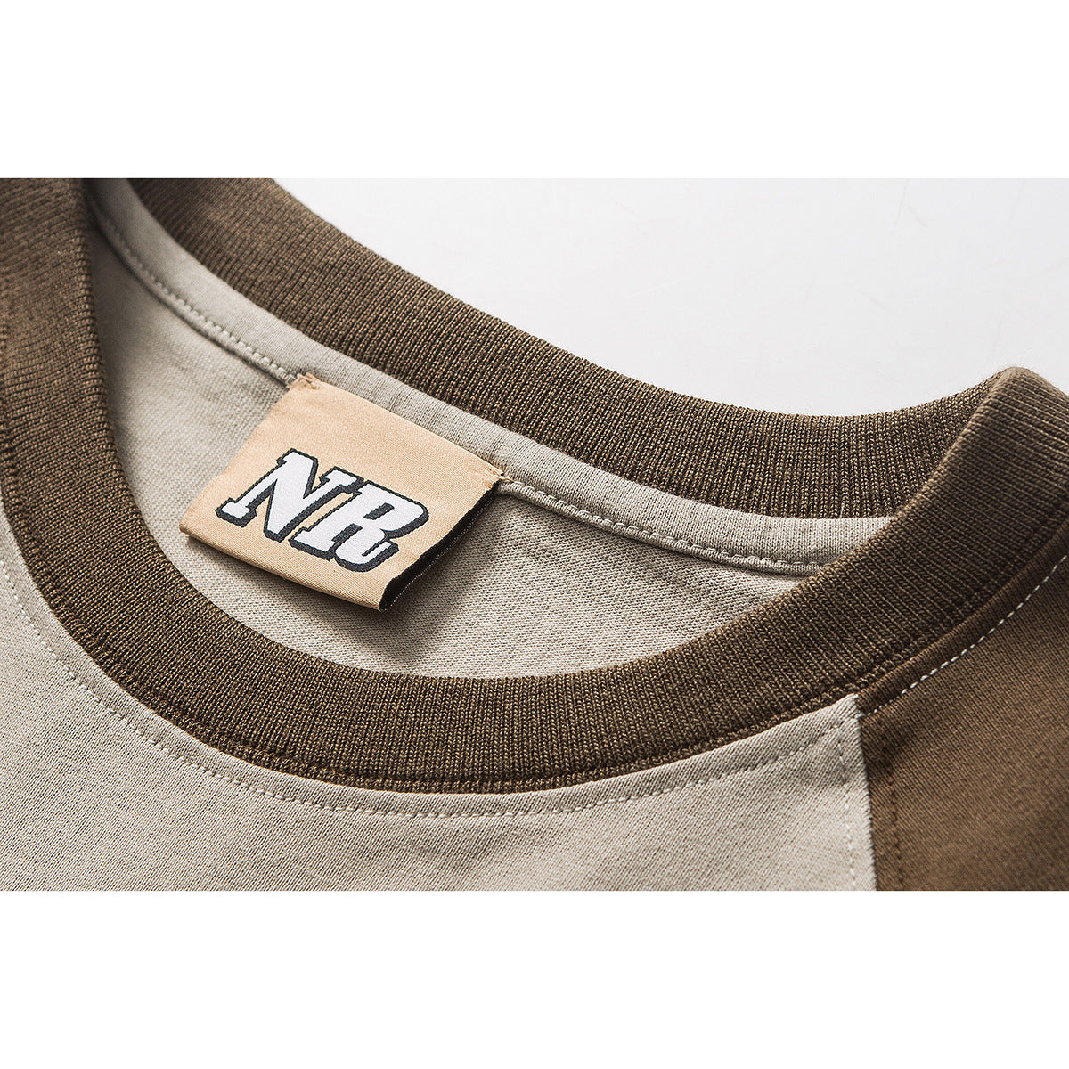 Close-up of a taupe T-shirt neckline with dark brown ribbed trim and a beige NB neck label.
