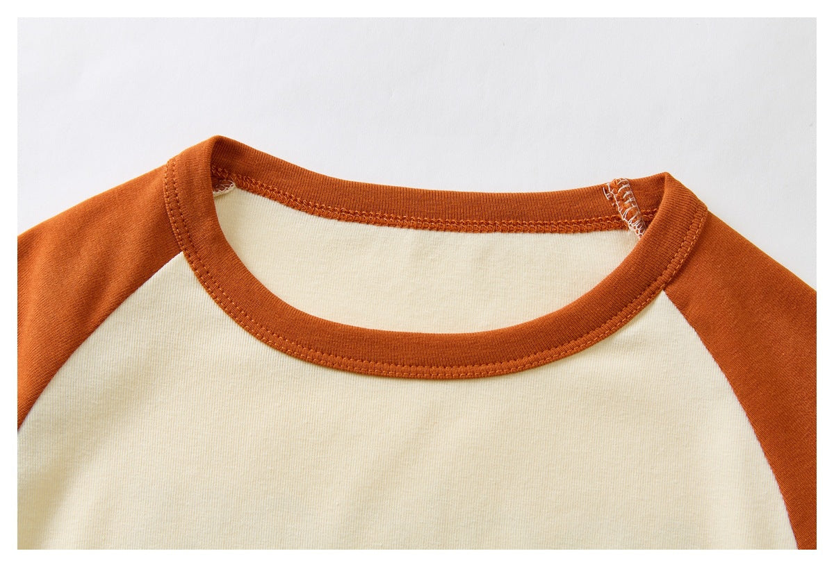 Close-up of a cream shirt body, rust-orange raglan sleeves, and stitched crew neckline.