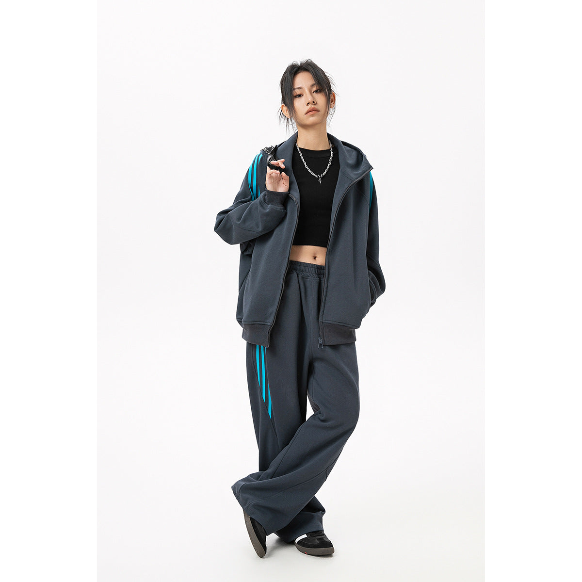 Model wearing a charcoal zip hoodie and wide-leg track pants with bright turquoise stripes.