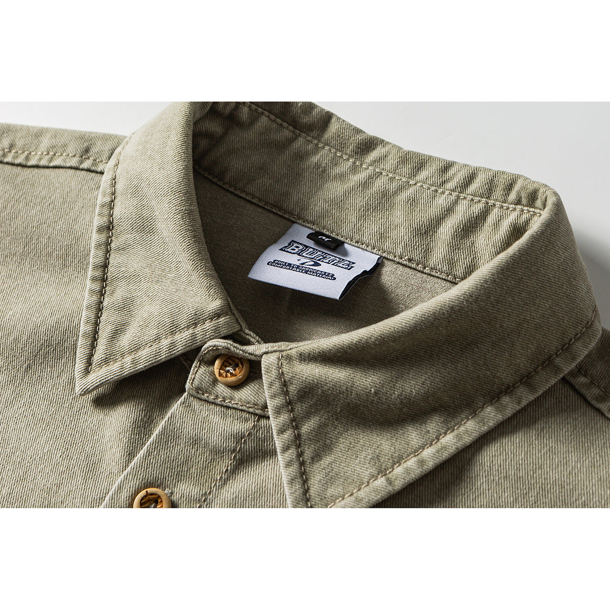 Close-up of an olive-gray shirt collar, tan buttons, stitching, and the sewn-in neck label.
