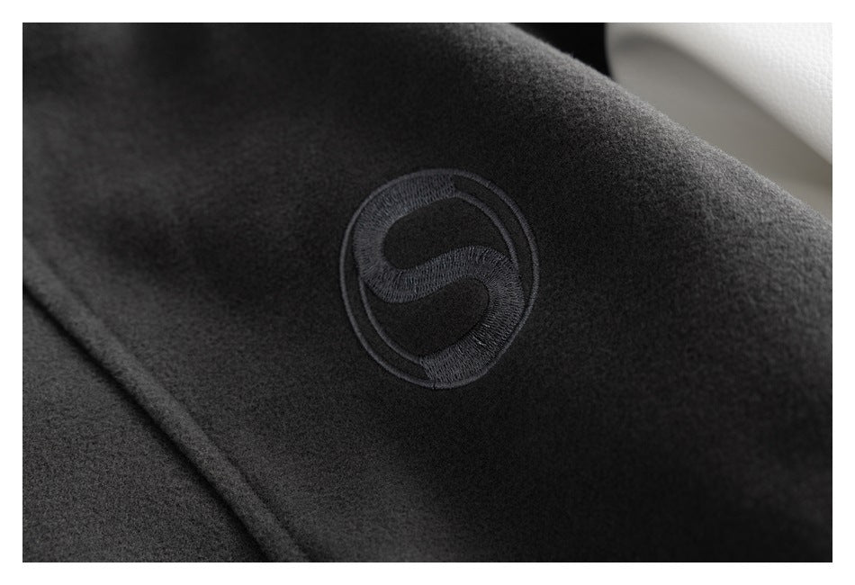 Close-up of a dark jacket with a circular black embroidered emblem on the fabric.