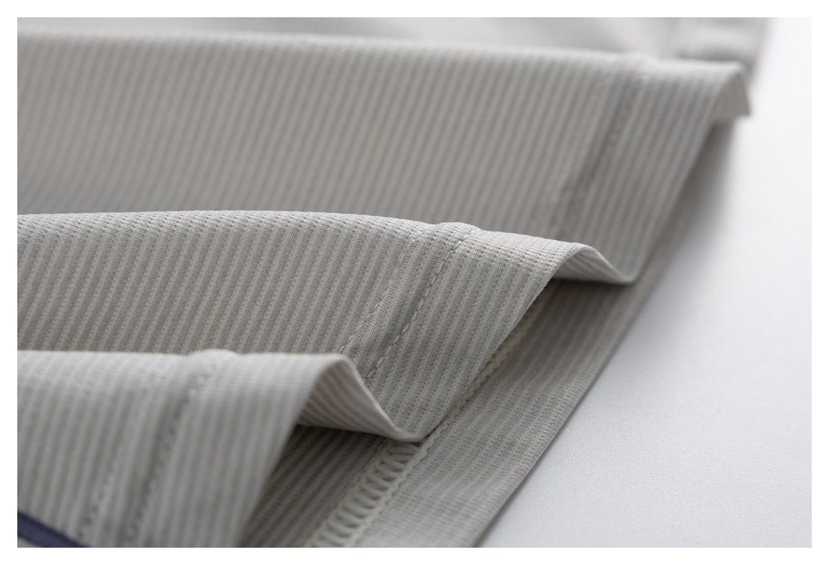Close-up of folded ivory garment edges with ribbed fabric, stitching, and a glimpse of lavender trim.