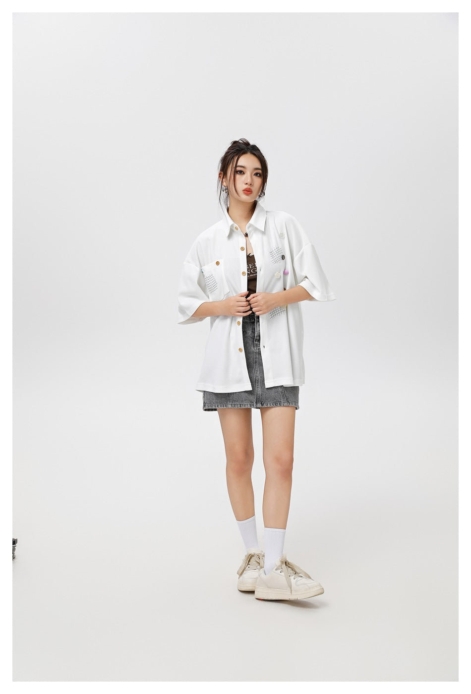 Model wearing the white oversized short-sleeve shirt open over a brown top with a gray denim mini skirt, full-length view