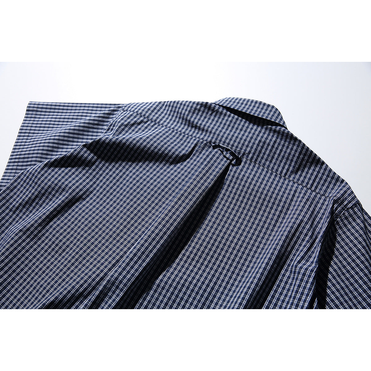 Close-up of the back yoke and pleat on a navy short-sleeve shirt with a white check pattern.