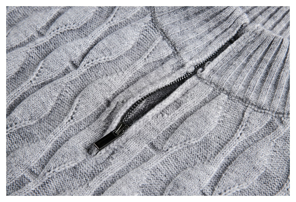 Close-up of a gray cable-knit sweater showing a black zipper and textured knit stitches.