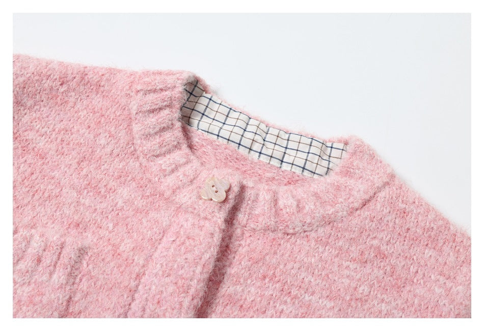 Close-up of a pink fuzzy knit neckline, beige button, and white plaid lining.