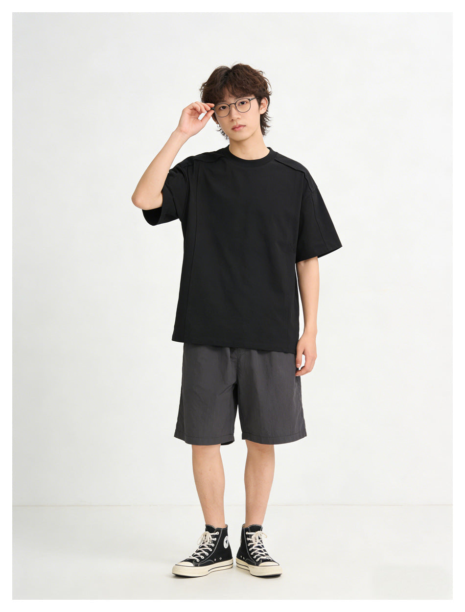 Model wearing a black relaxed crew-neck T-shirt with gray shorts and black high-top sneakers, front view