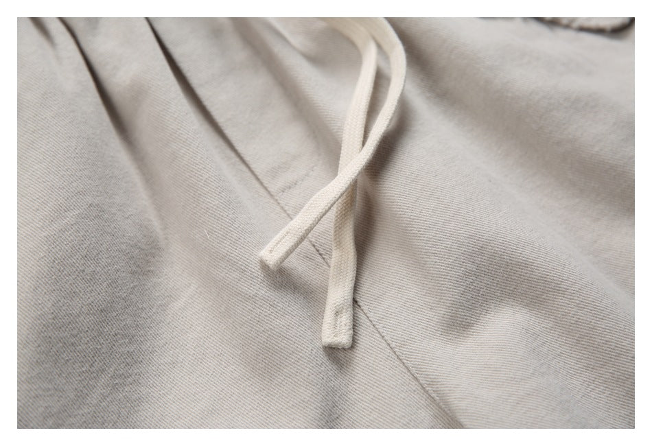 Close-up of the beige pants' drawstrings, fabric texture and stitching.