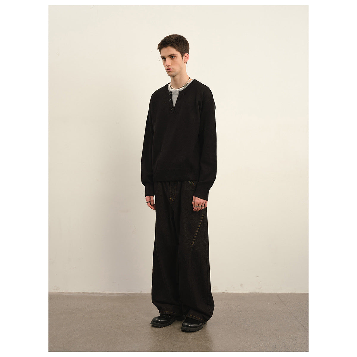 Model wearing a black long-sleeve henley sweater and wide-leg black trousers, shown full length.
