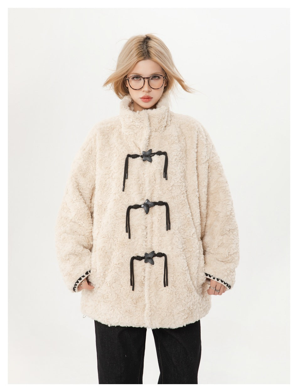 Model wearing an ivory plush coat with a high collar, three black toggle closures, and black trousers, front view.