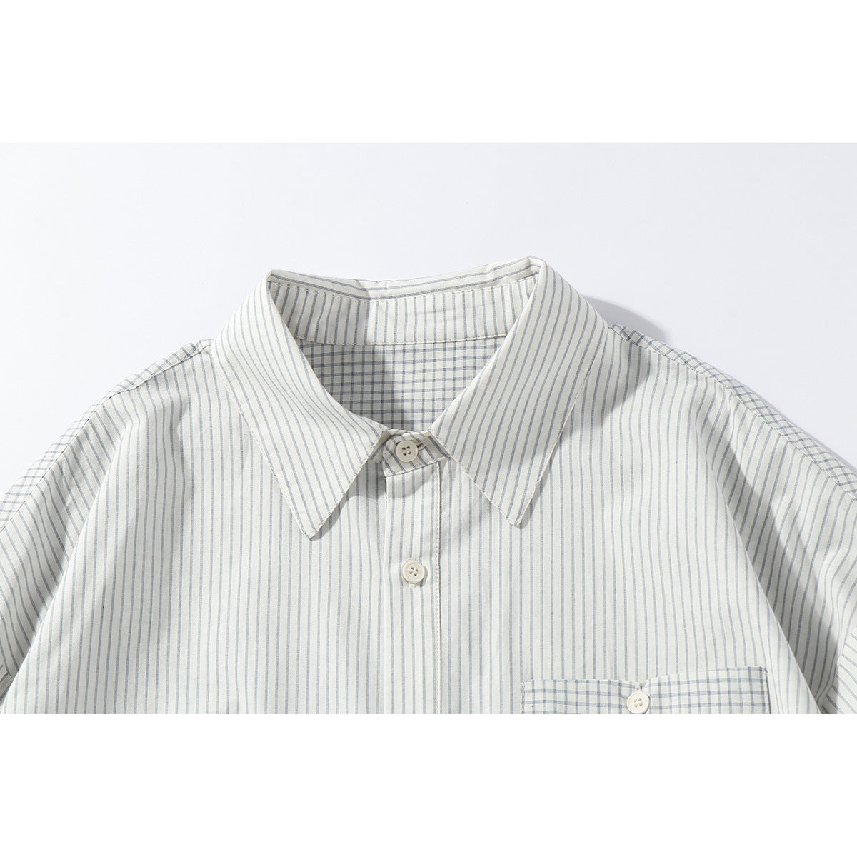 Close-up of an off-white shirt with fine gray vertical stripes, pointed collar, buttons, and a checked inner yoke.