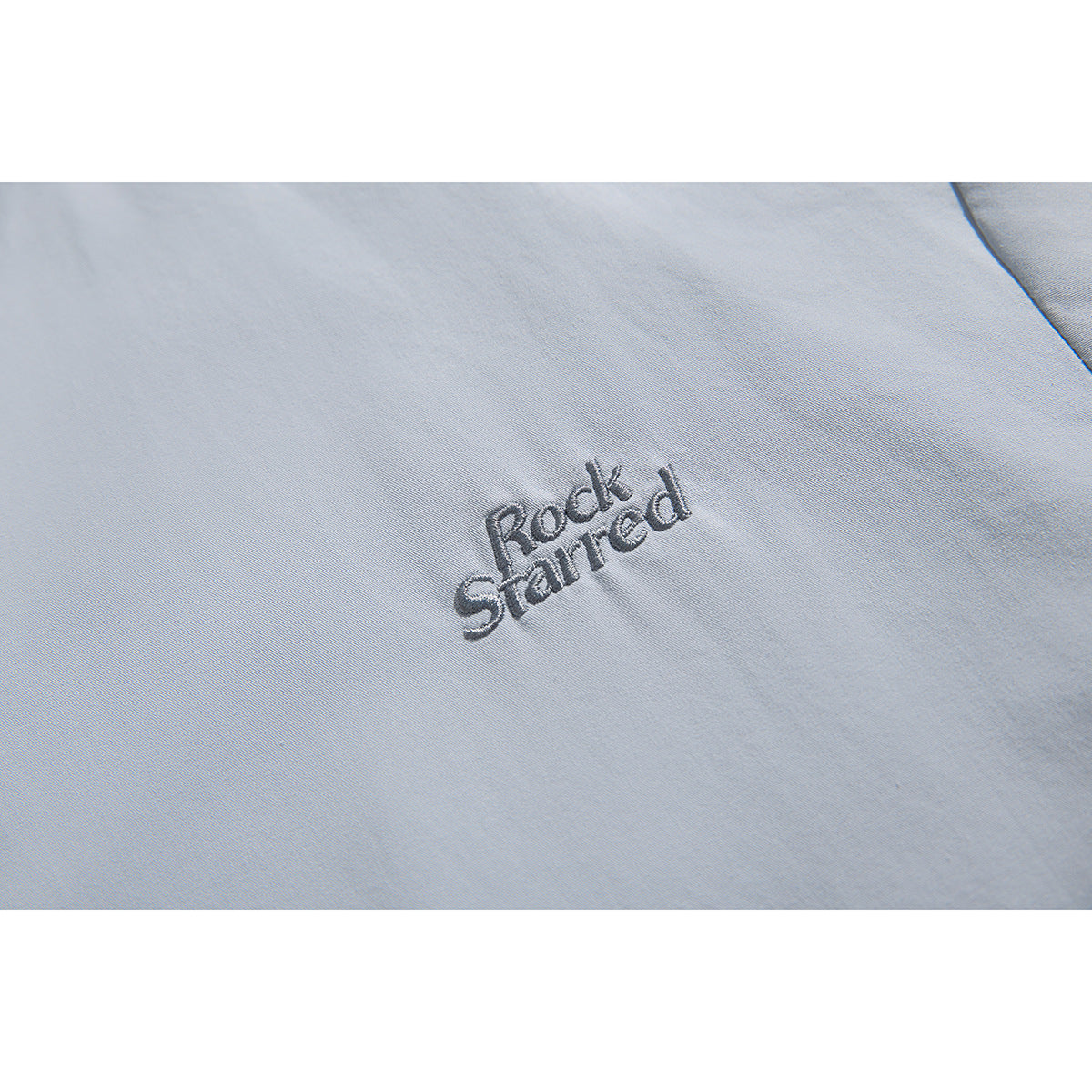 Close-up of dark embroidered lettering on light blue-gray jacket fabric.