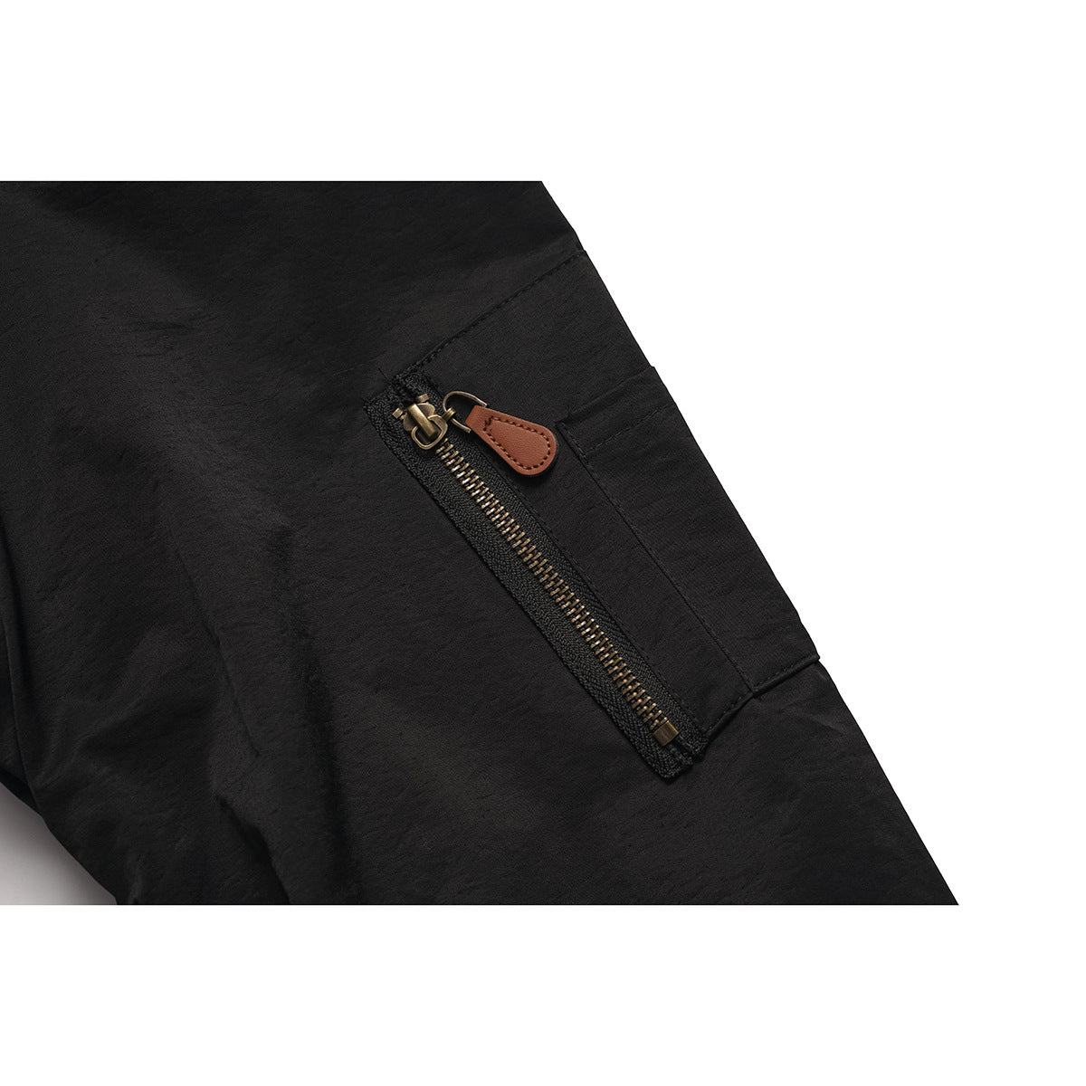 Close-up of a black jacket's diagonal sleeve zipper pocket with brass-tone teeth and a brown pull tab.