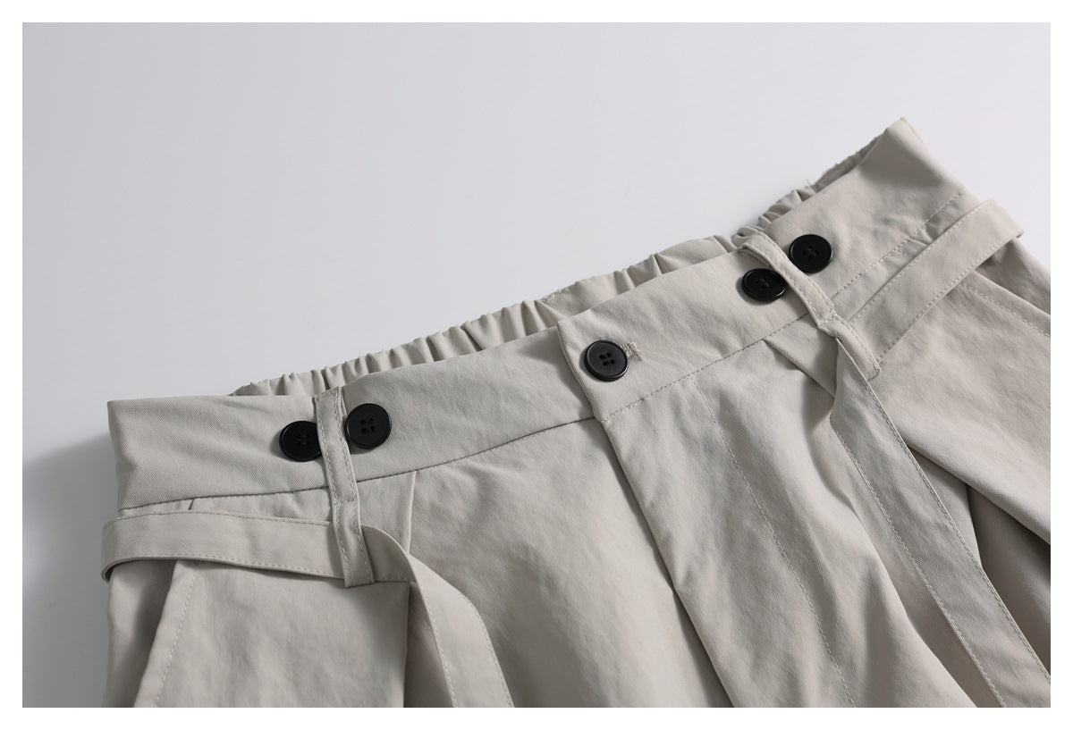 Close-up of the light beige trousers' gathered waistband, black buttons, belt loops and matching belt.