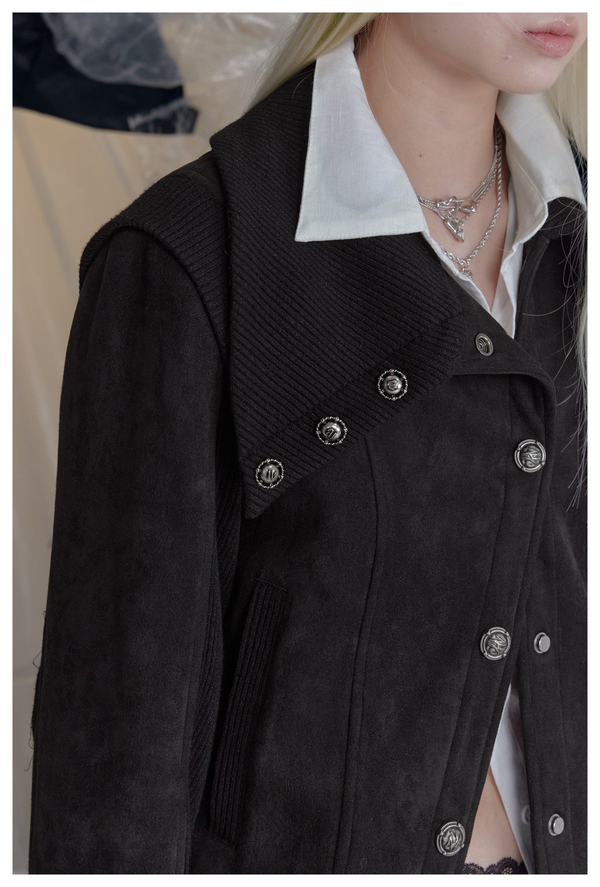 Close-up of a person wearing a black jacket with ribbed panels and ornate silver buttons over a white collared shirt.