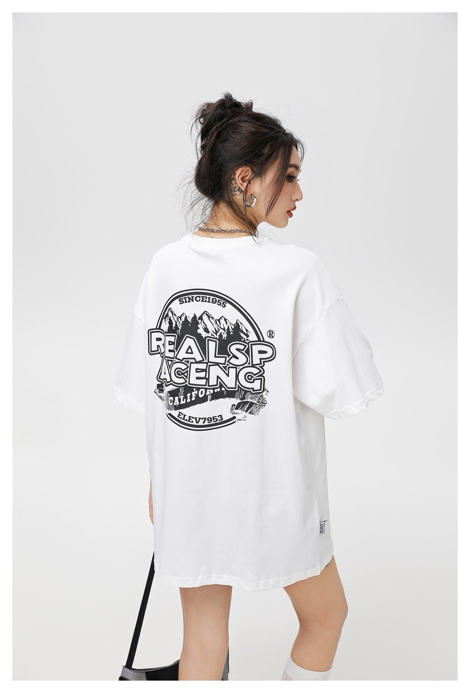 Model viewed from behind in an oversized white T-shirt with a large black mountain-and-lettering back graphic.