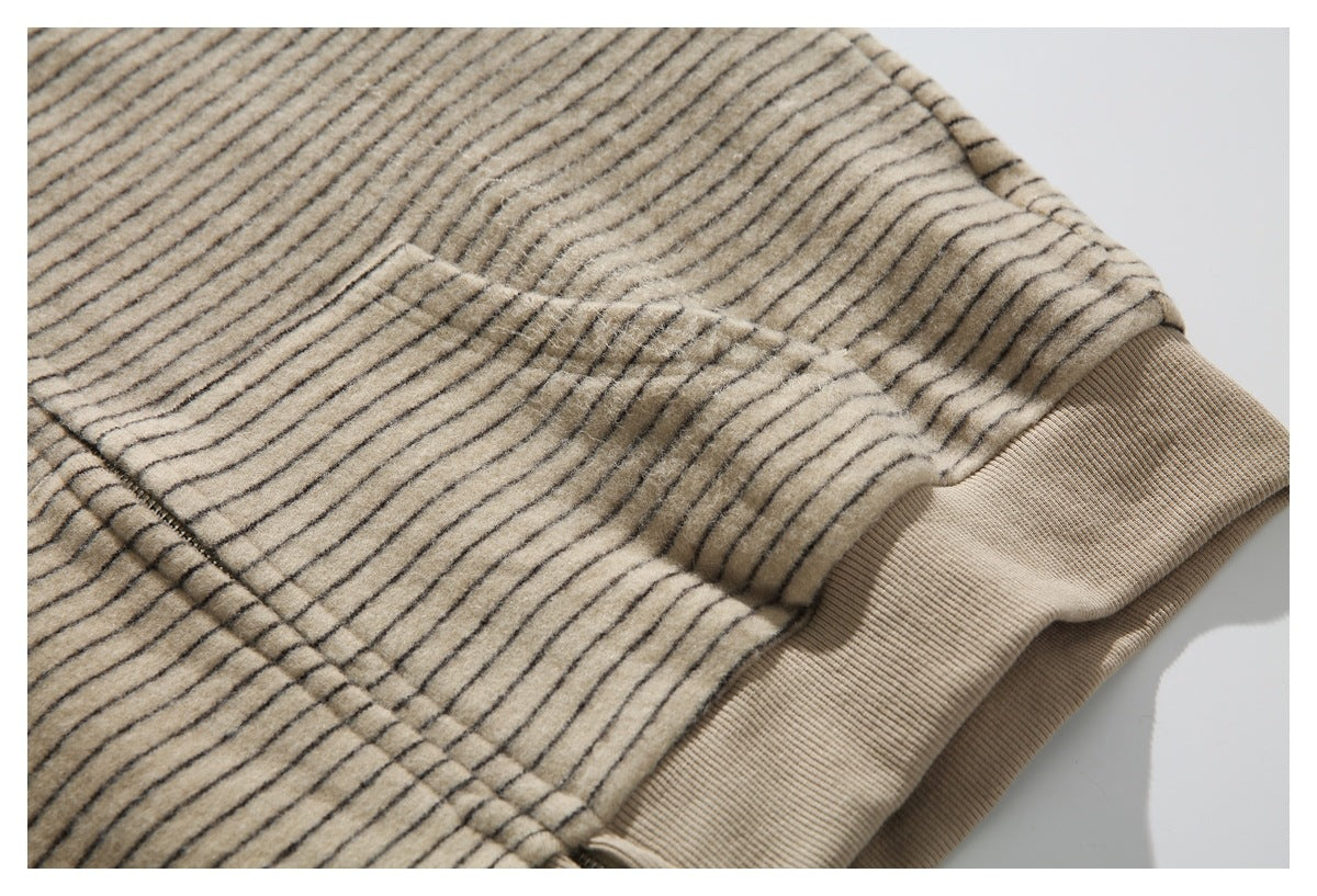 Close-up of a seam and pocket area on a beige jacket with thin dark stripes and a ribbed hem.