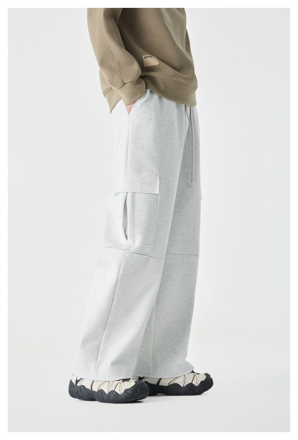 Cropped model in light gray wide-leg cargo pants with flap pockets, shown from the side with a beige sweatshirt.