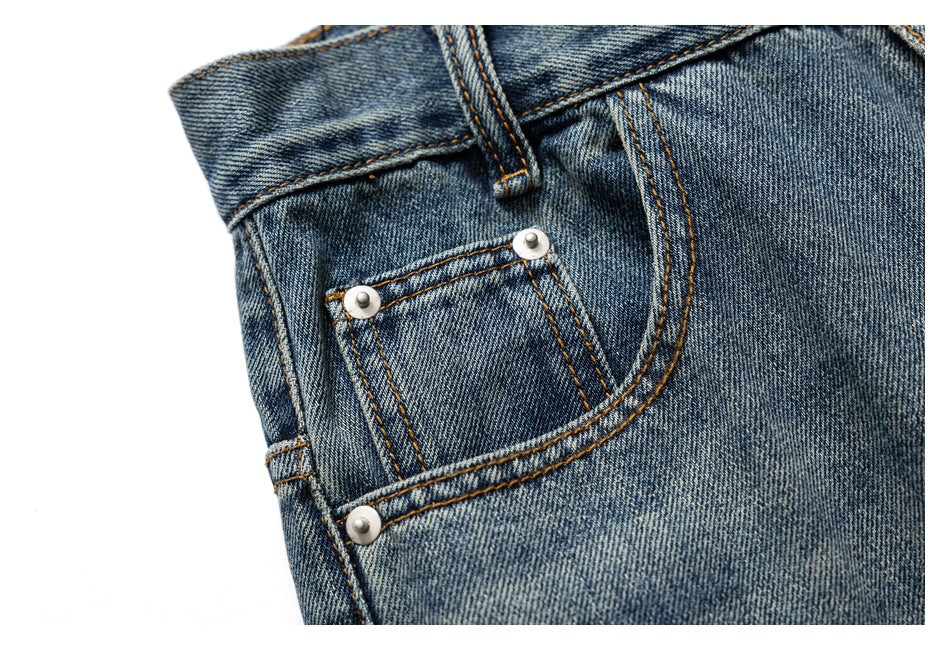 Close-up of the front coin pocket, rivets, belt loop and curved pocket stitching on blue-wash jeans.