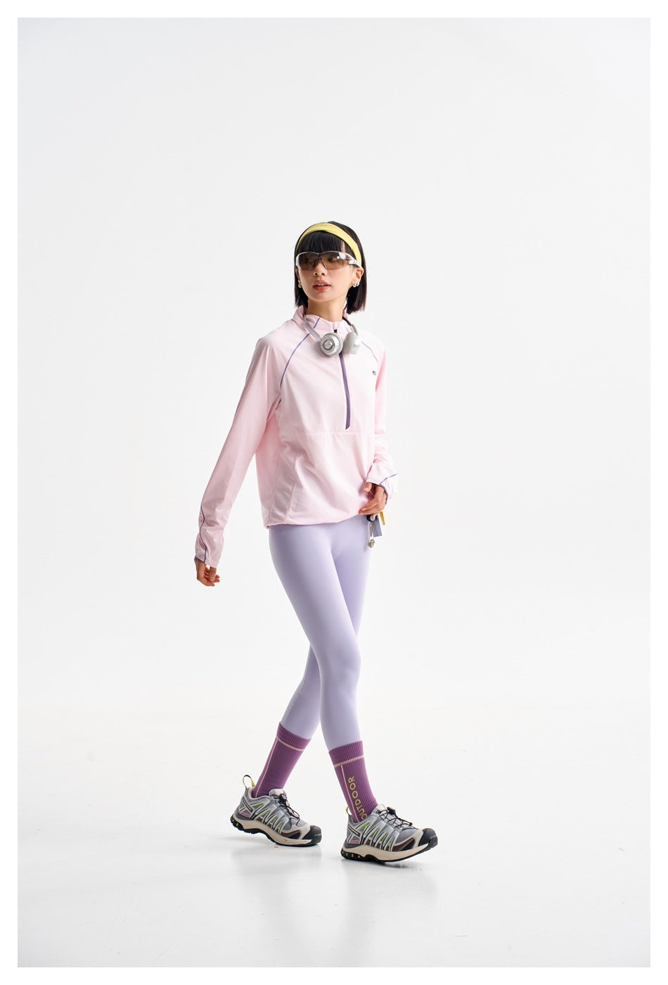 Model walking in a pale pink quarter-zip top and pale lavender leggings.
