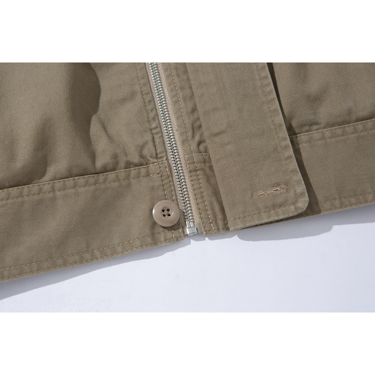 Close-up of a taupe jacket hem showing a metal zipper, button, and stitched panel.