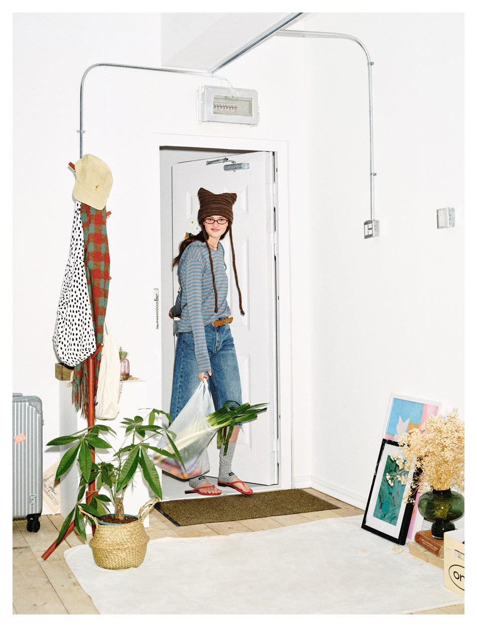 Woman in a striped long-sleeve top and jeans stepping through a doorway carrying a shopping bag