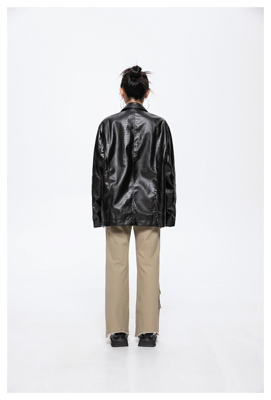 Back view of a model wearing a black crocodile-textured blazer with beige trousers.