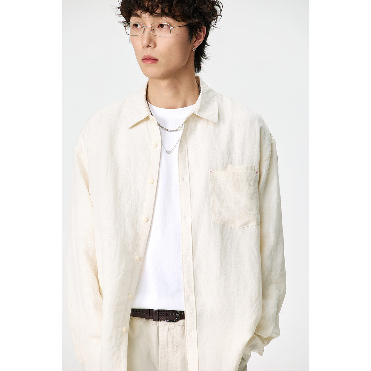 Close view of a model wearing an open ivory button-up shirt with a chest pocket over a white T-shirt.