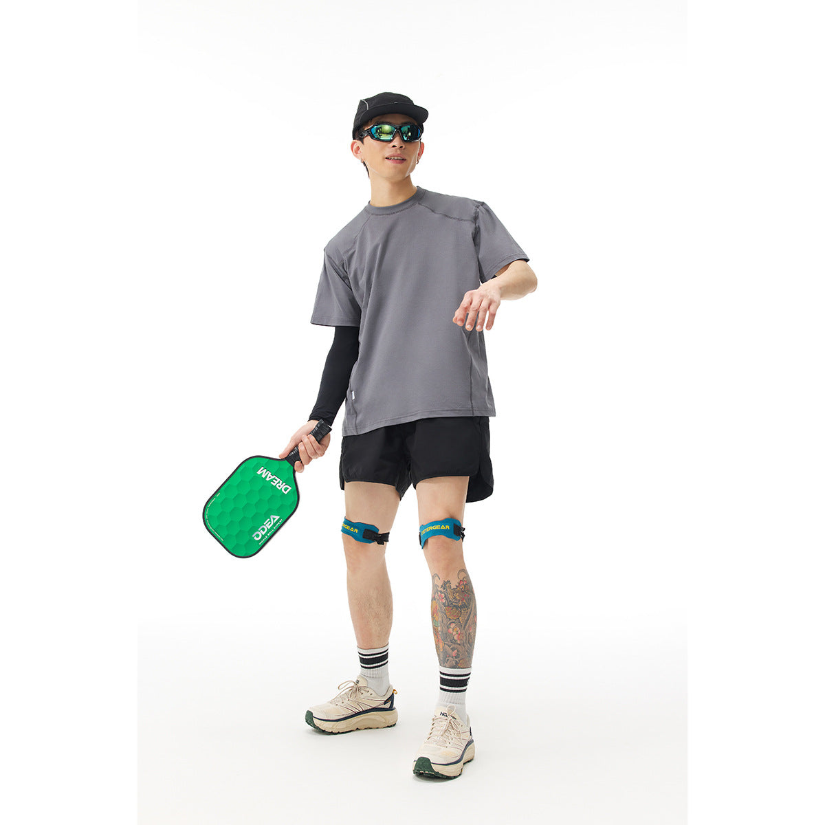 Model wearing a gray short-sleeve T-shirt and black shorts, holding a green paddle against a white background.