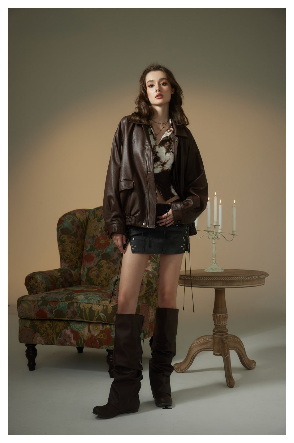 Model wearing coffee brown faux-leather jacket over a printed top with black lace-up mini skirt and brown boots
