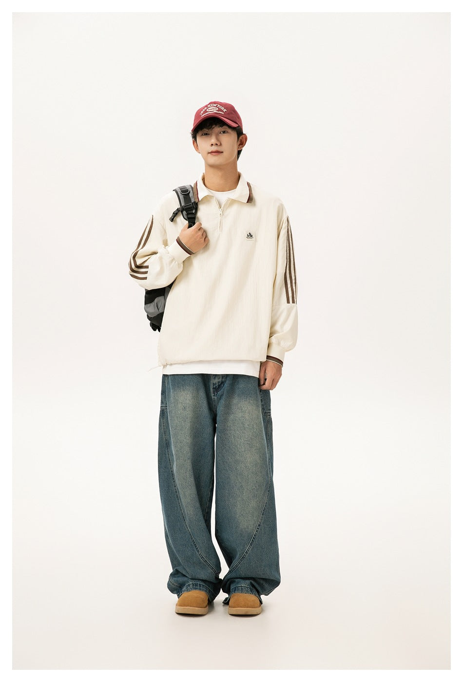Model wearing a cream quarter-zip polo-collar jacket with brown stripes, red cap, backpack and wide-leg jeans