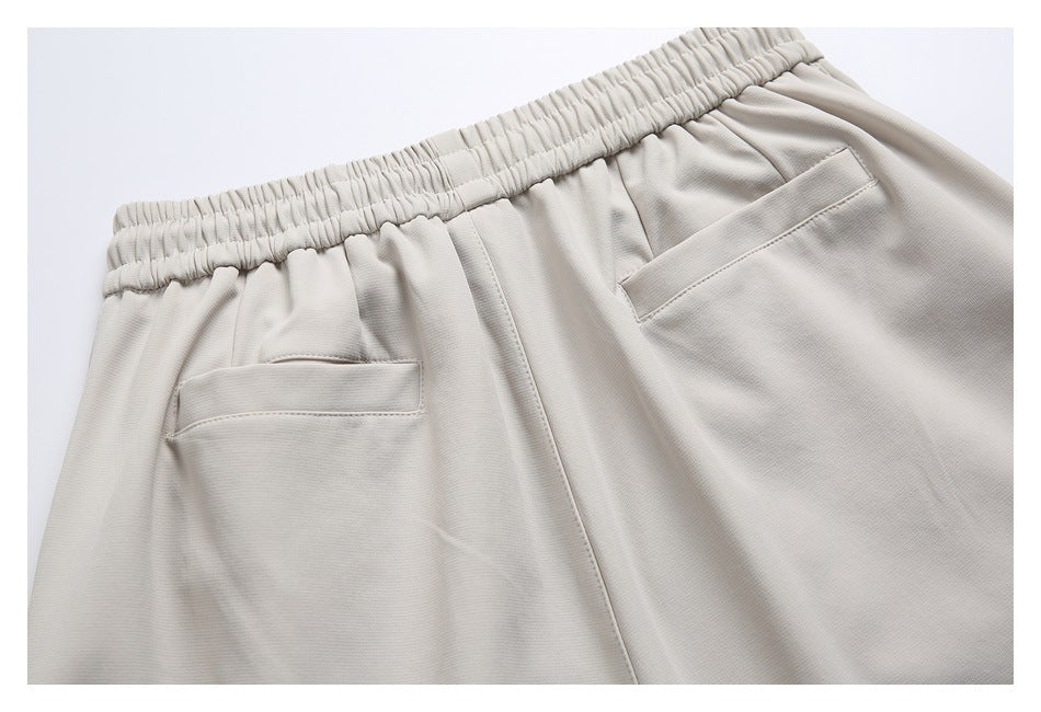 Close-up of the back waist of light beige trousers, showing an elastic waistband and two welt pockets.