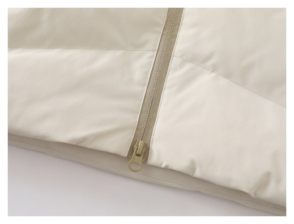Close-up of a tan zipper ending near the hem of a cream jacket.