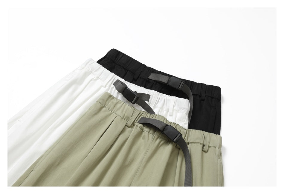 Three pairs of trousers in black, white, and sage green arranged together, each with an elastic waist and dark webbing belt.