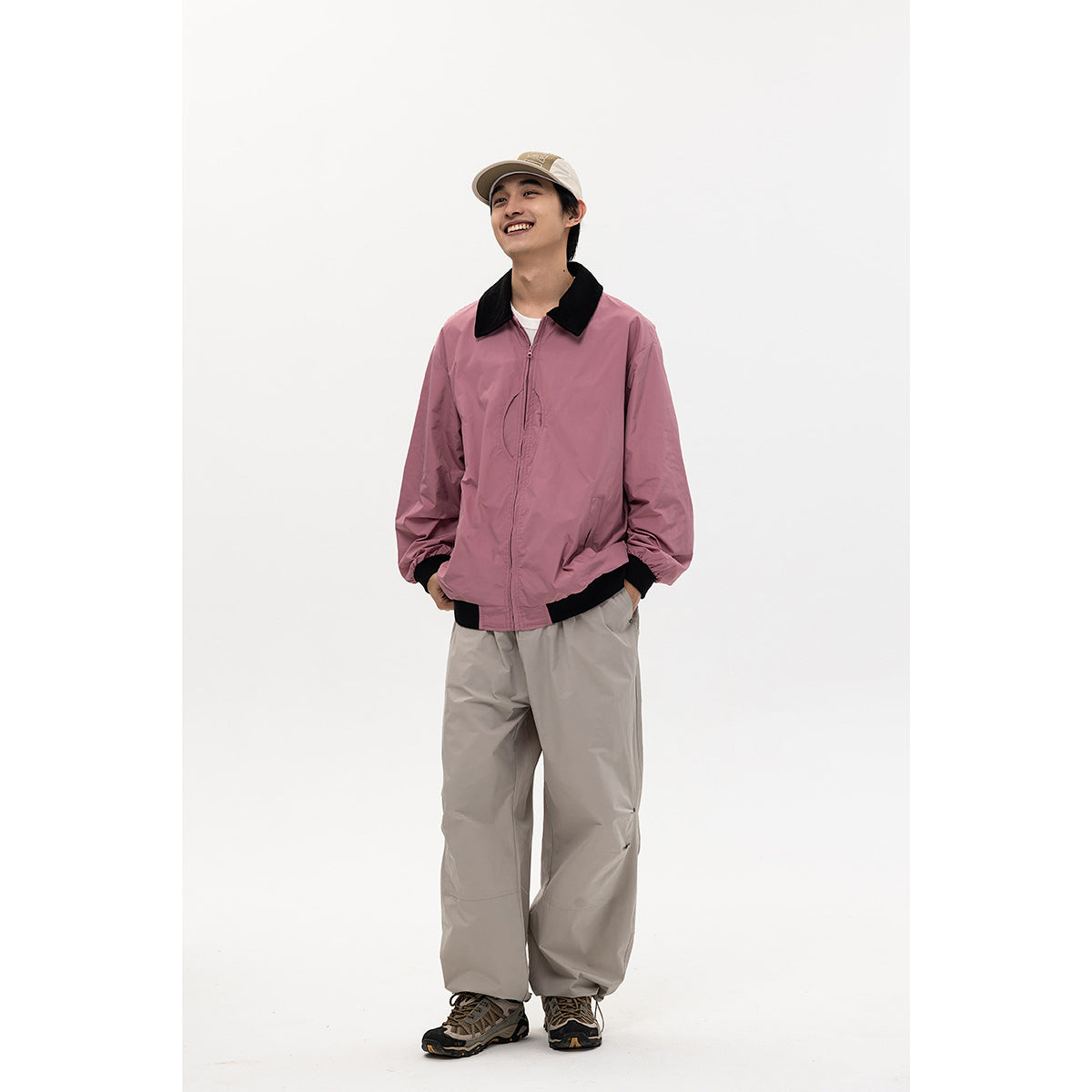 Full-length model wearing a pink jacket with black collar and trim, light trousers, and a beige cap.