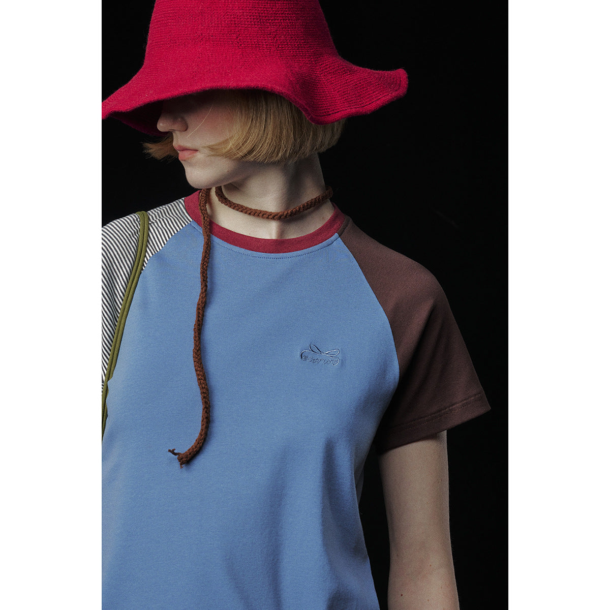 Close front view of a model wearing a blue raglan T-shirt with brown and striped sleeves and a red hat.