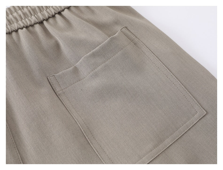 Close-up of a large rectangular patch pocket stitched onto taupe trousers.
