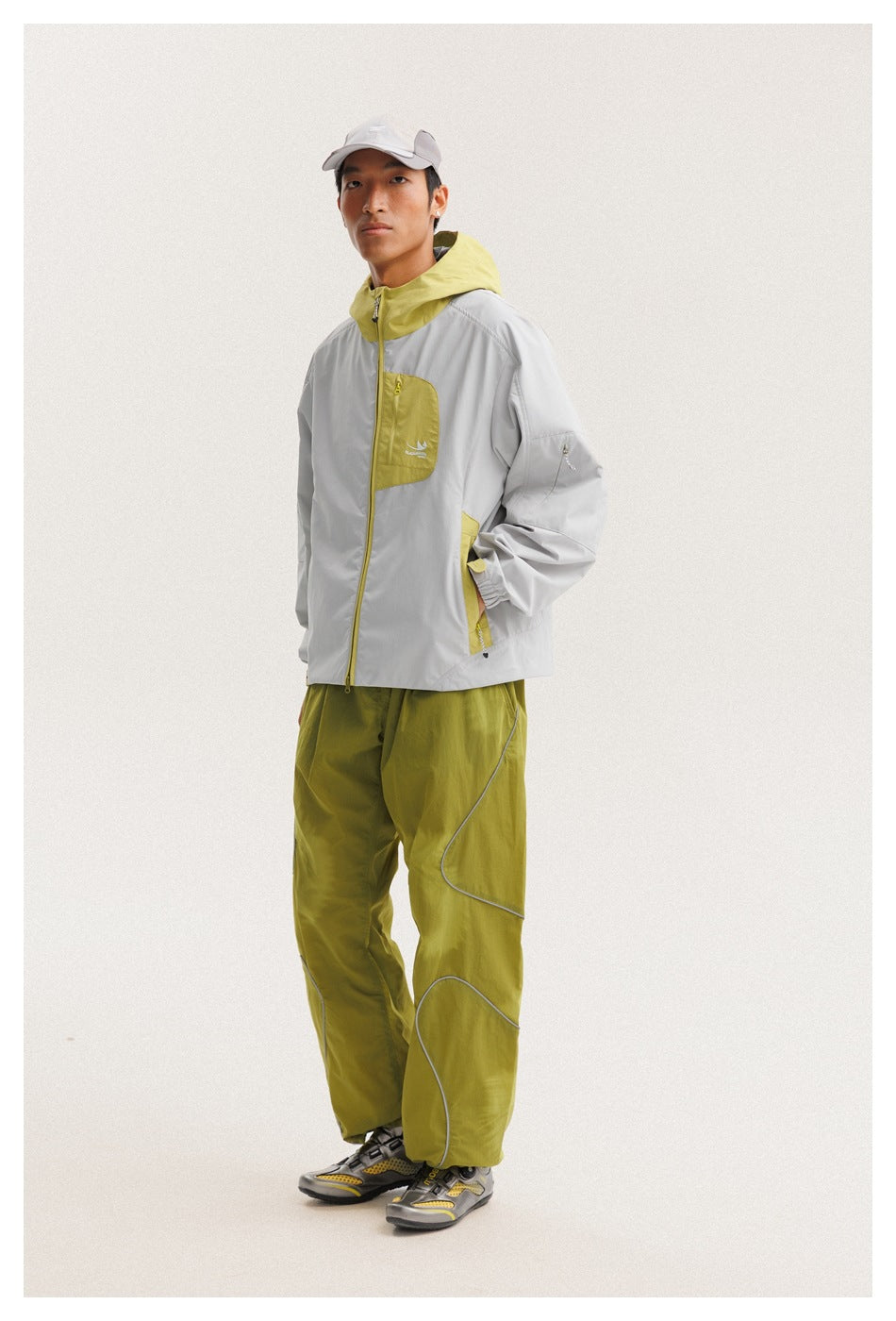 Model in a light gray jacket with yellow-green accents and olive trousers, shown at a three-quarter angle.